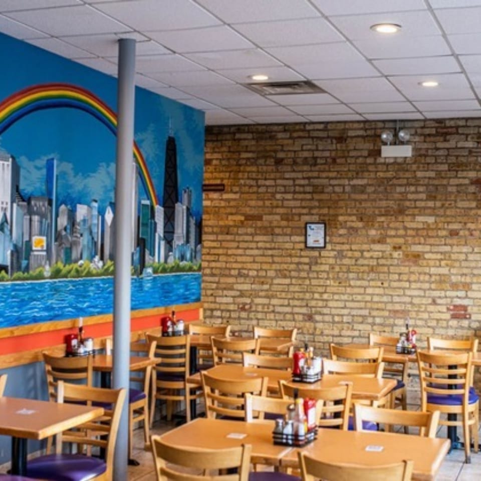 Interior of Stella's Diner with wooden tables and chairs, a brick wall, and a city mural.