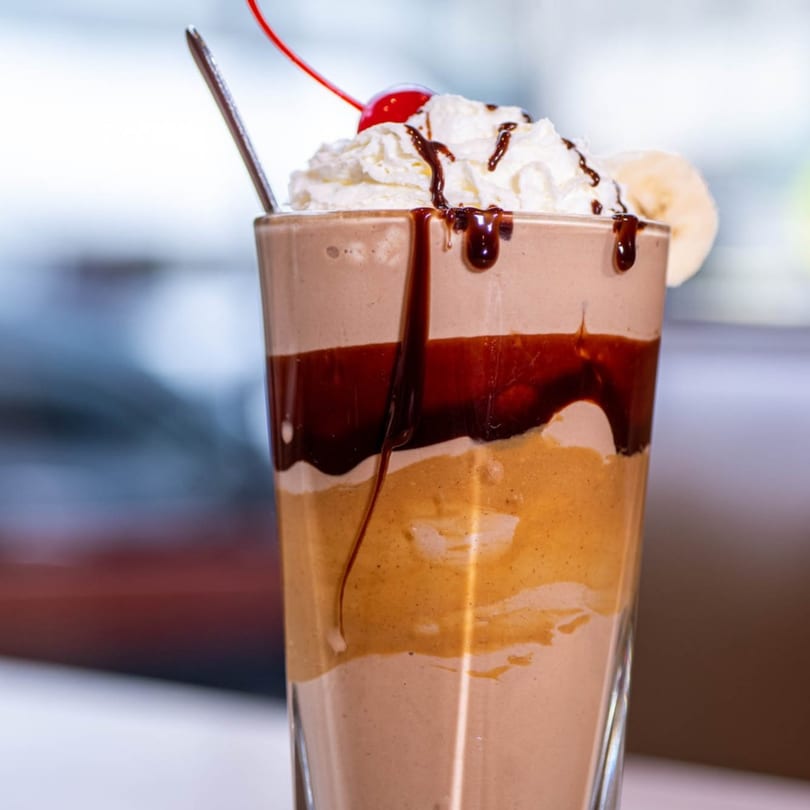 A Stella's Diner milkshake with chocolate, peanut butter, whipped cream, cherry, and banana slice.