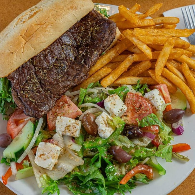 Stella's Diner steak sandwich with fries and a fresh Greek salad on a white plate.